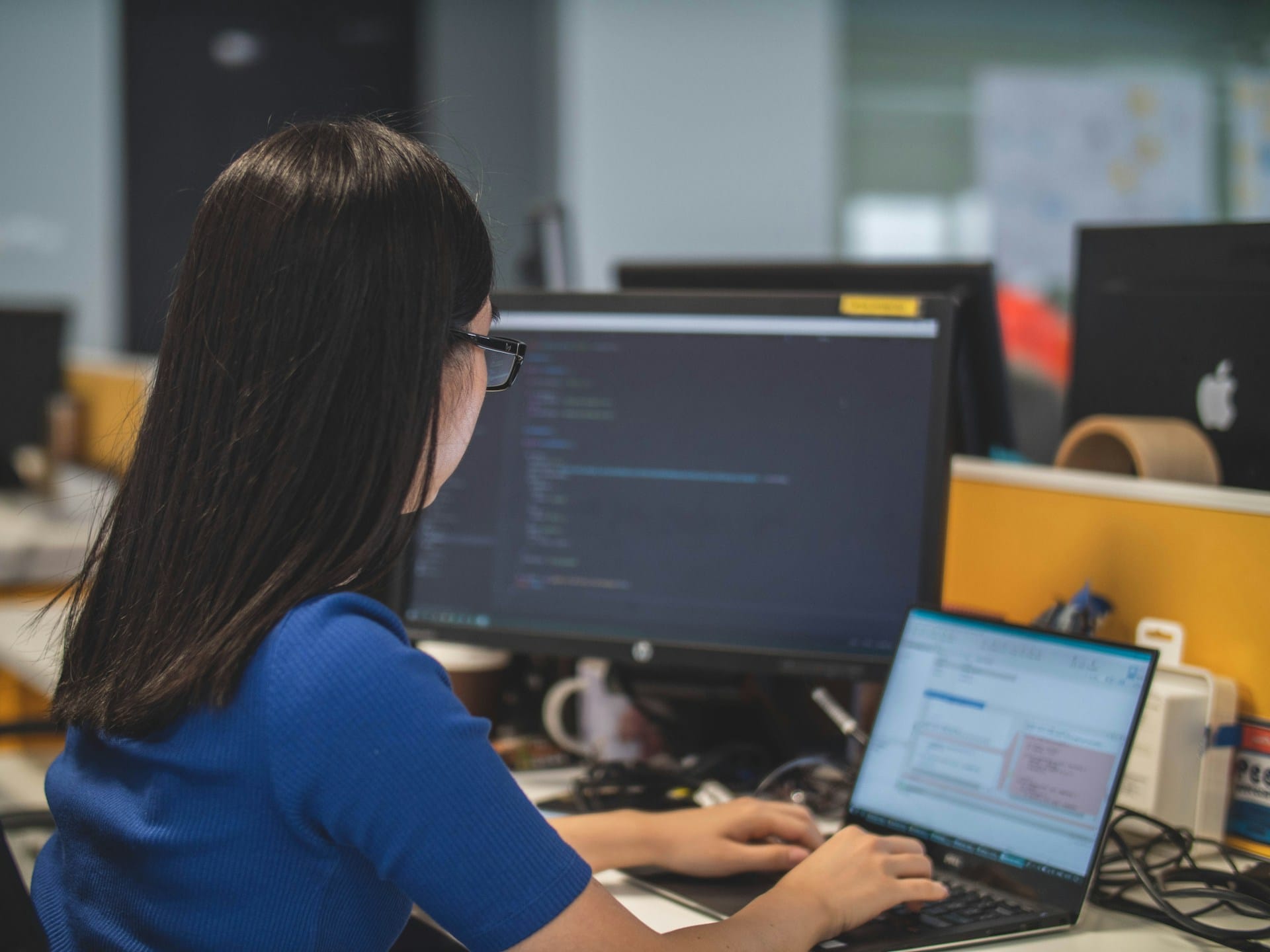 An office worker working on a laptop and a monitor at an office desk
