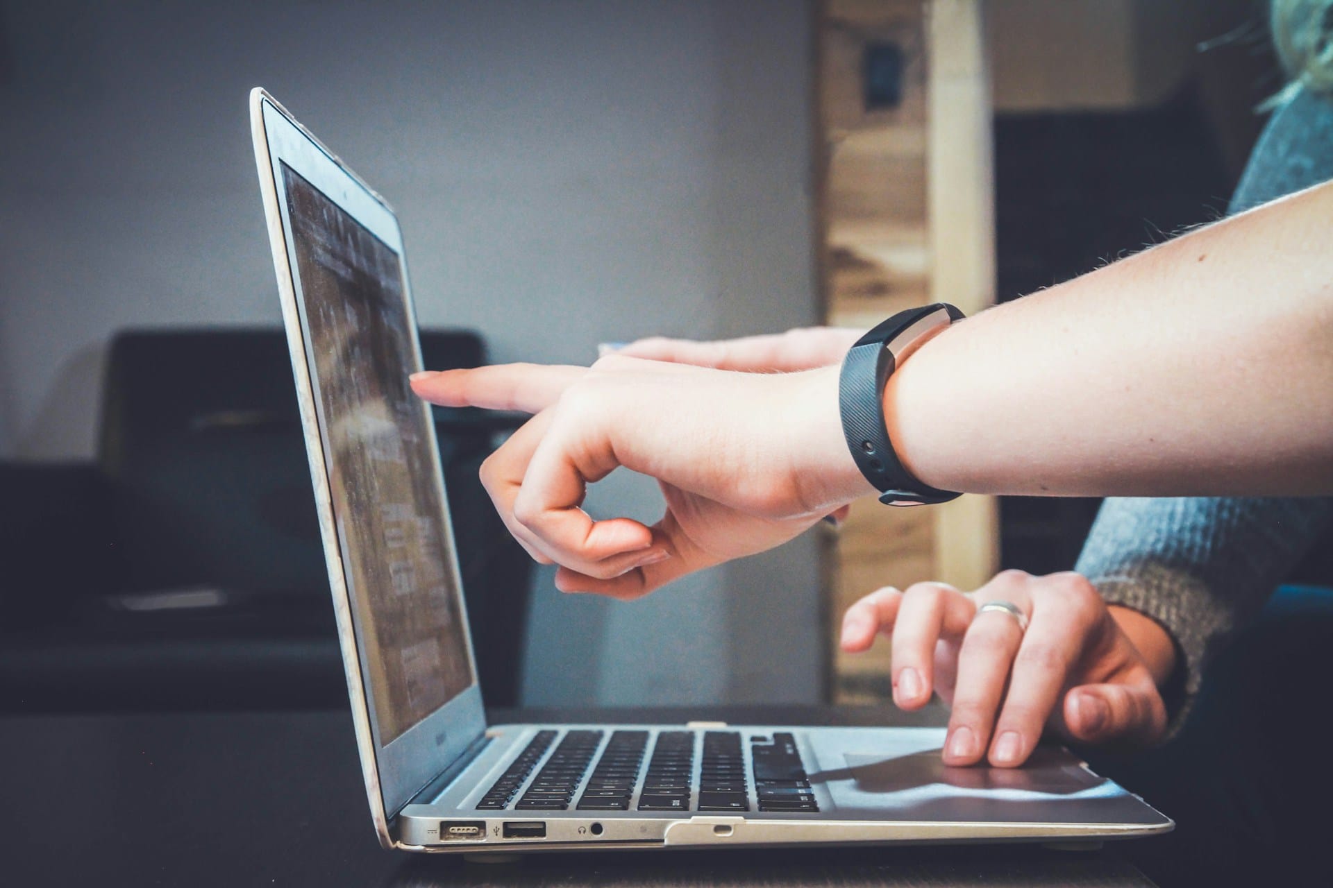 A side view of a laptop on a table, with the hands of two colleagues visible as they point to the screen 