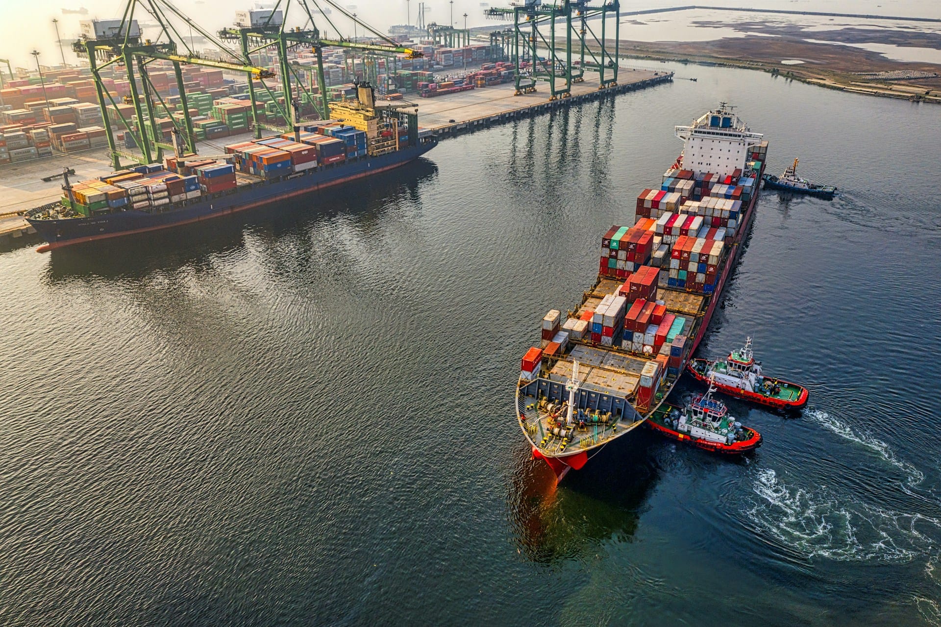 An aerial view of a large export ship leaving a shipping yard, stacked high with containers