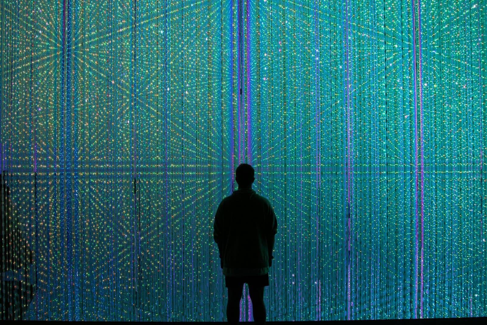 A black silhouette of a person standing in the centre, looking at a large abstract display of digital data 