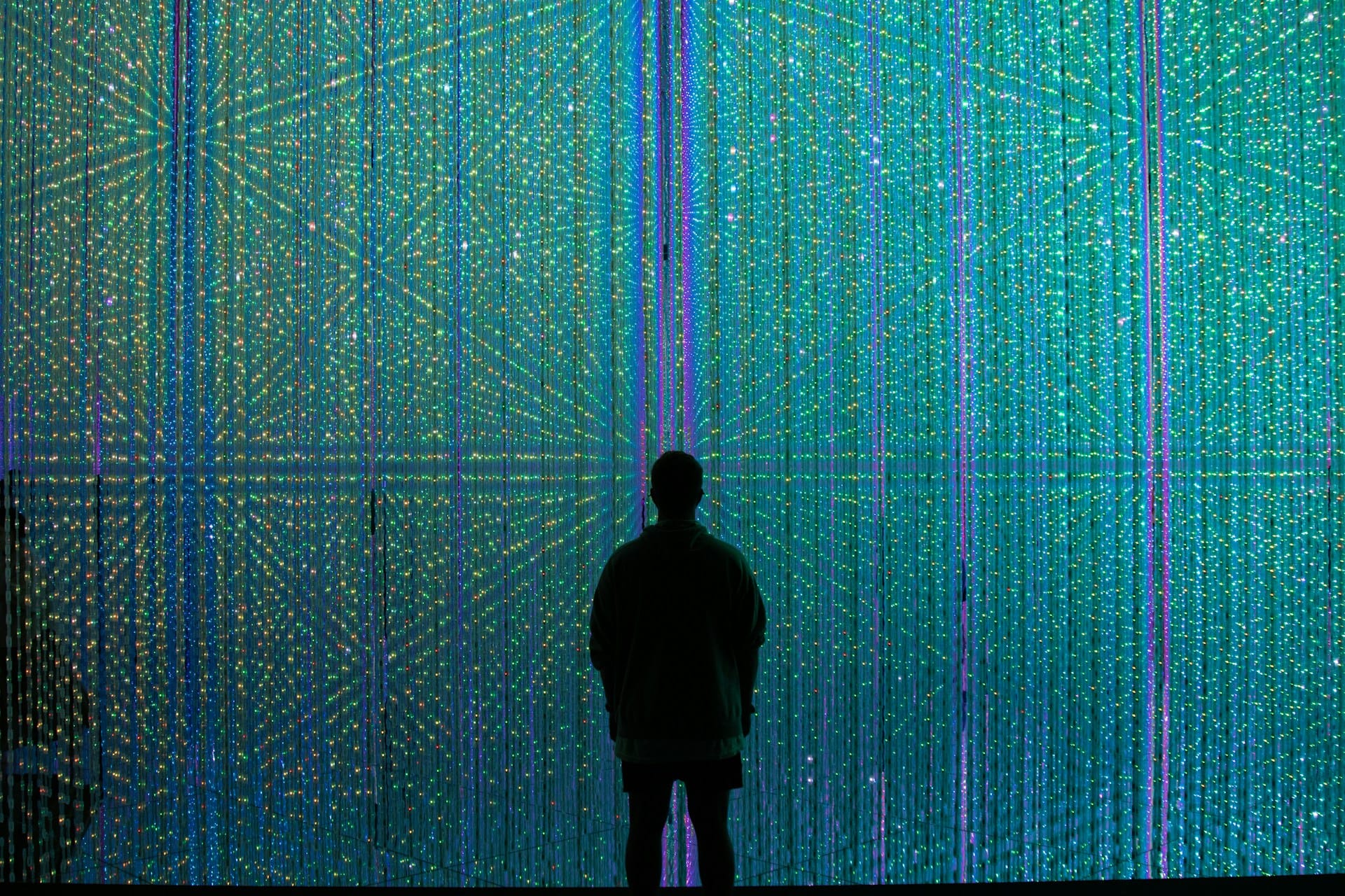 A black silhouette of a person standing in the centre, looking at a large abstract display of digital data 